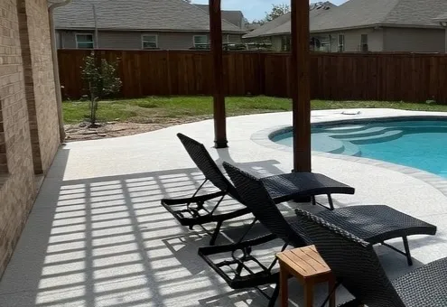 Covered patio lounge area beside a pool finished with light speckled TPV rubber surfacing