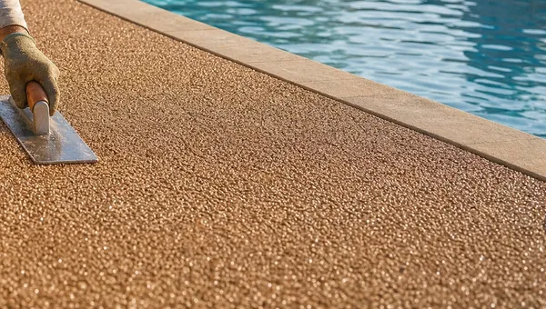 Close-up of a hand trowel smoothing fresh TPV rubber granules along a pool deck edge